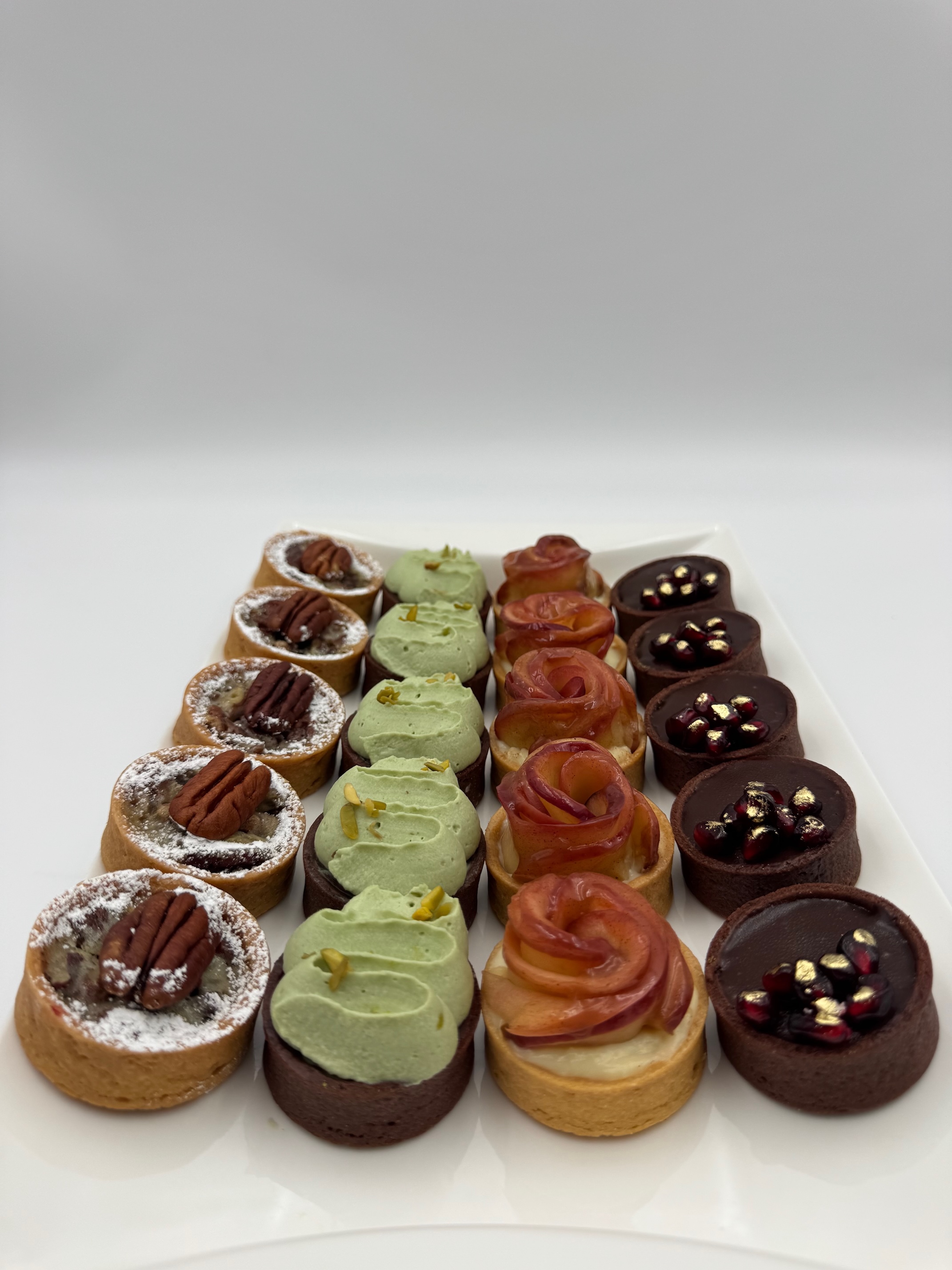 Assorted mini tart desserts with chocolate, pistachio, pecan, and apple toppings