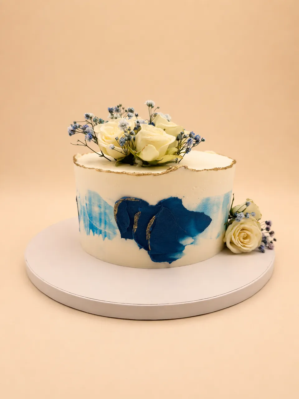 Blue and white floral cake with fresh roses, gold edge, and abstract blue buttercream design