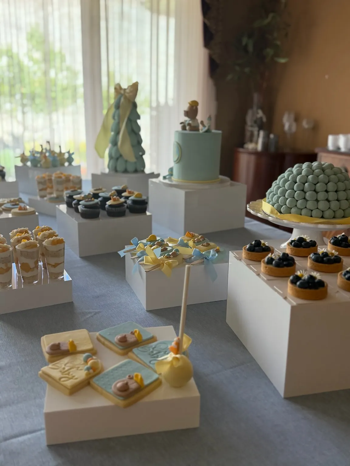 Blue and yellow baby shower dessert table with cake, tarts, sweet shots, and cookies