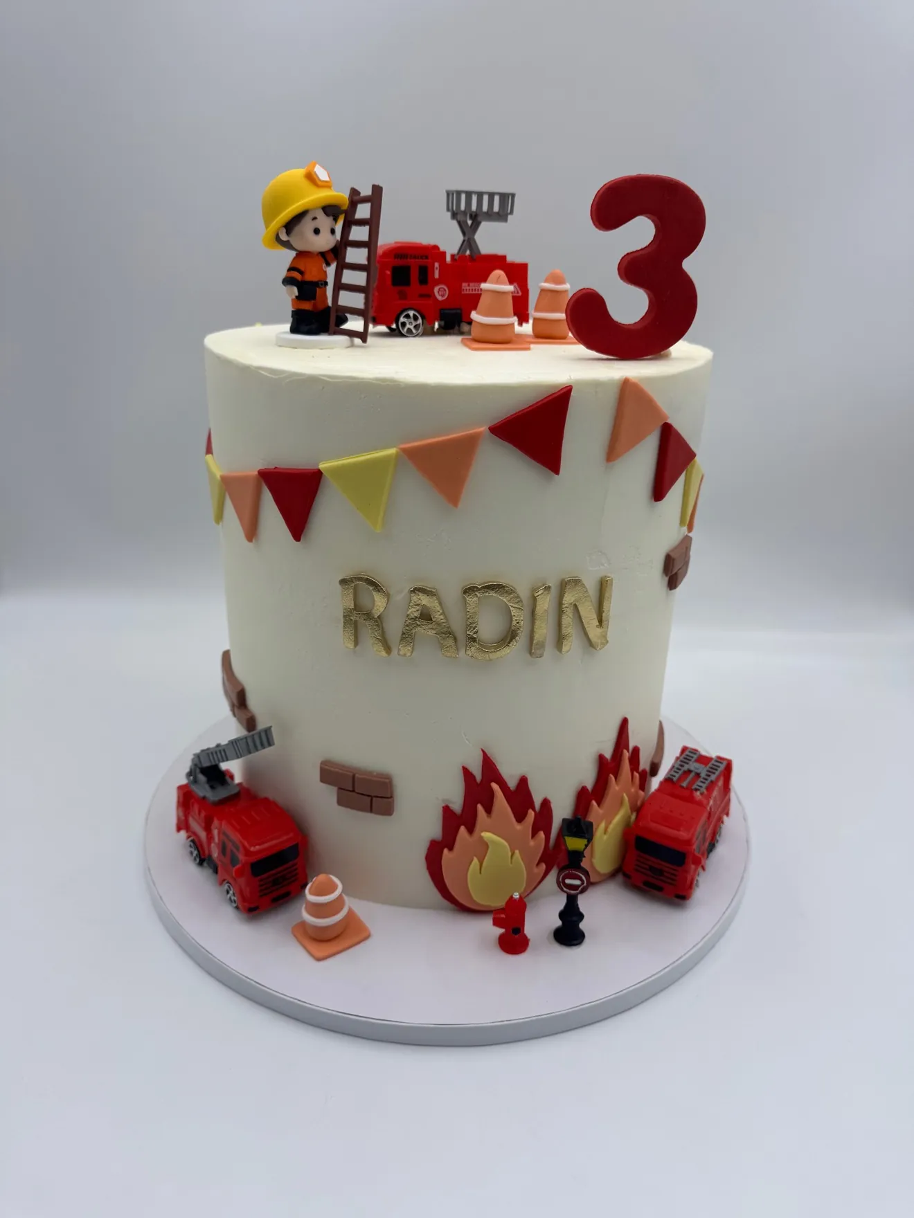 Firefighter third birthday cake with fire trucks, flames, and construction banner