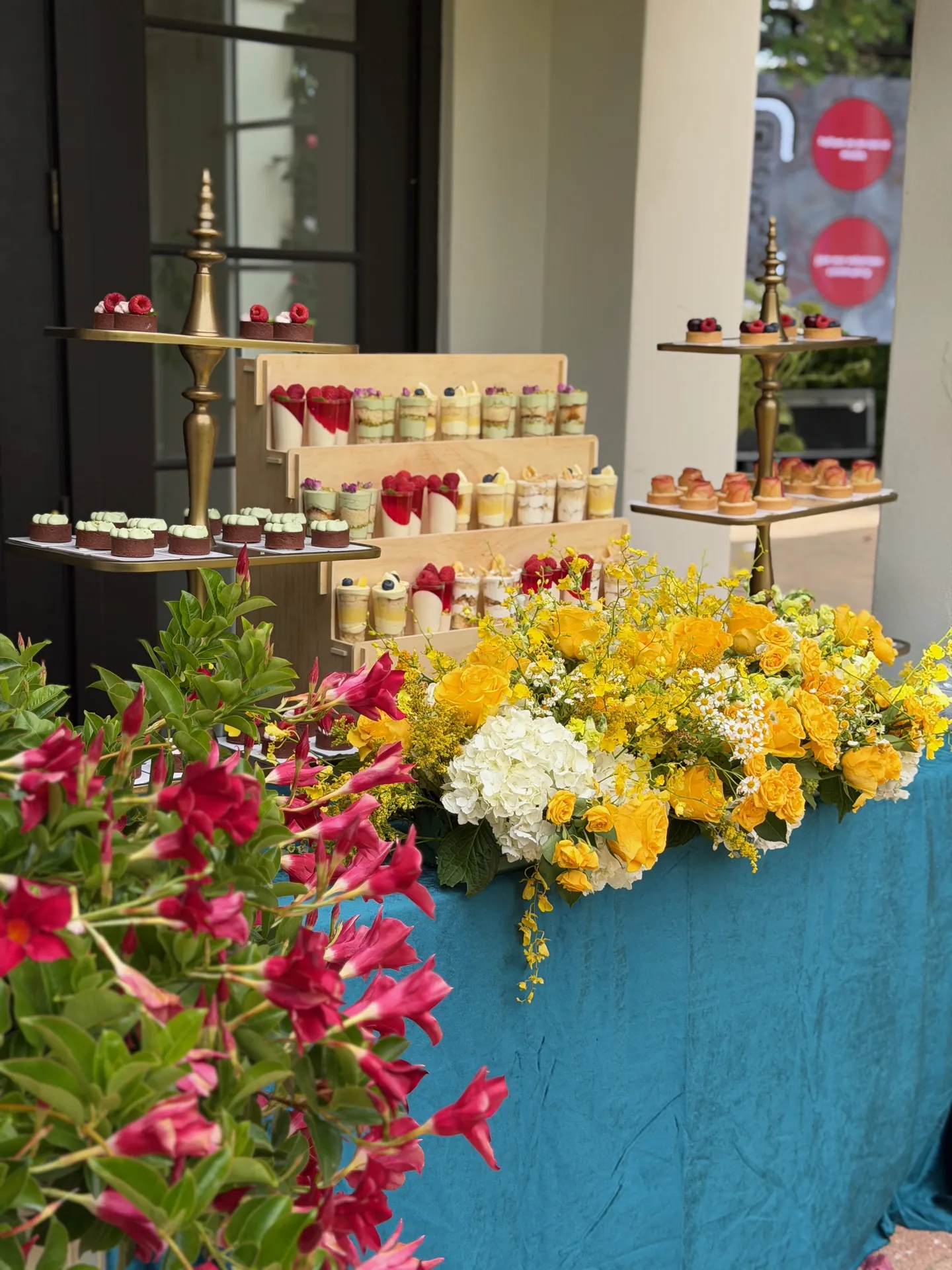 Sweet table with mini desserts, gold stands, and a yellow floral arrangement