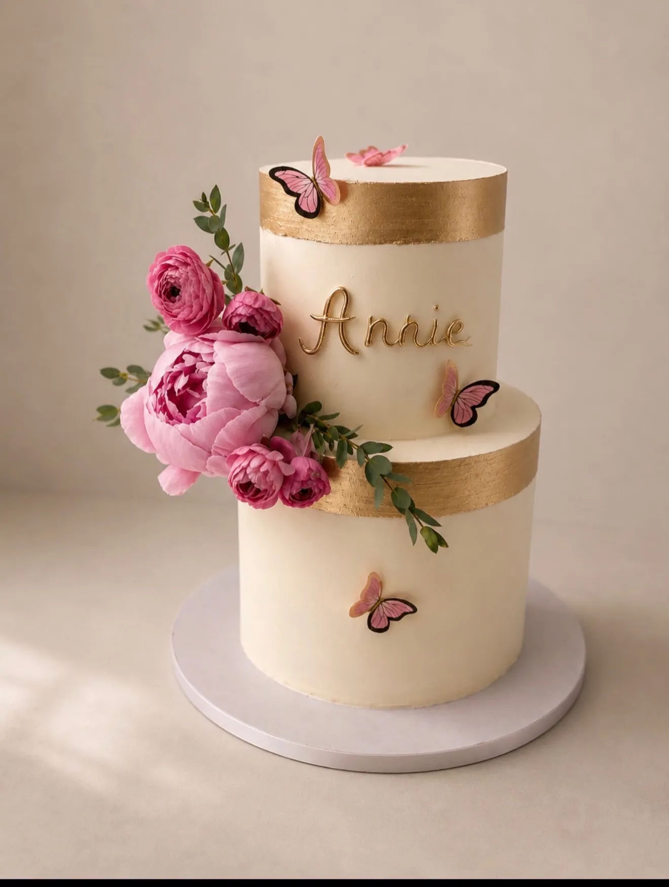 Gold and ivory custom cake with pink peonies, butterflies, and custom name topper