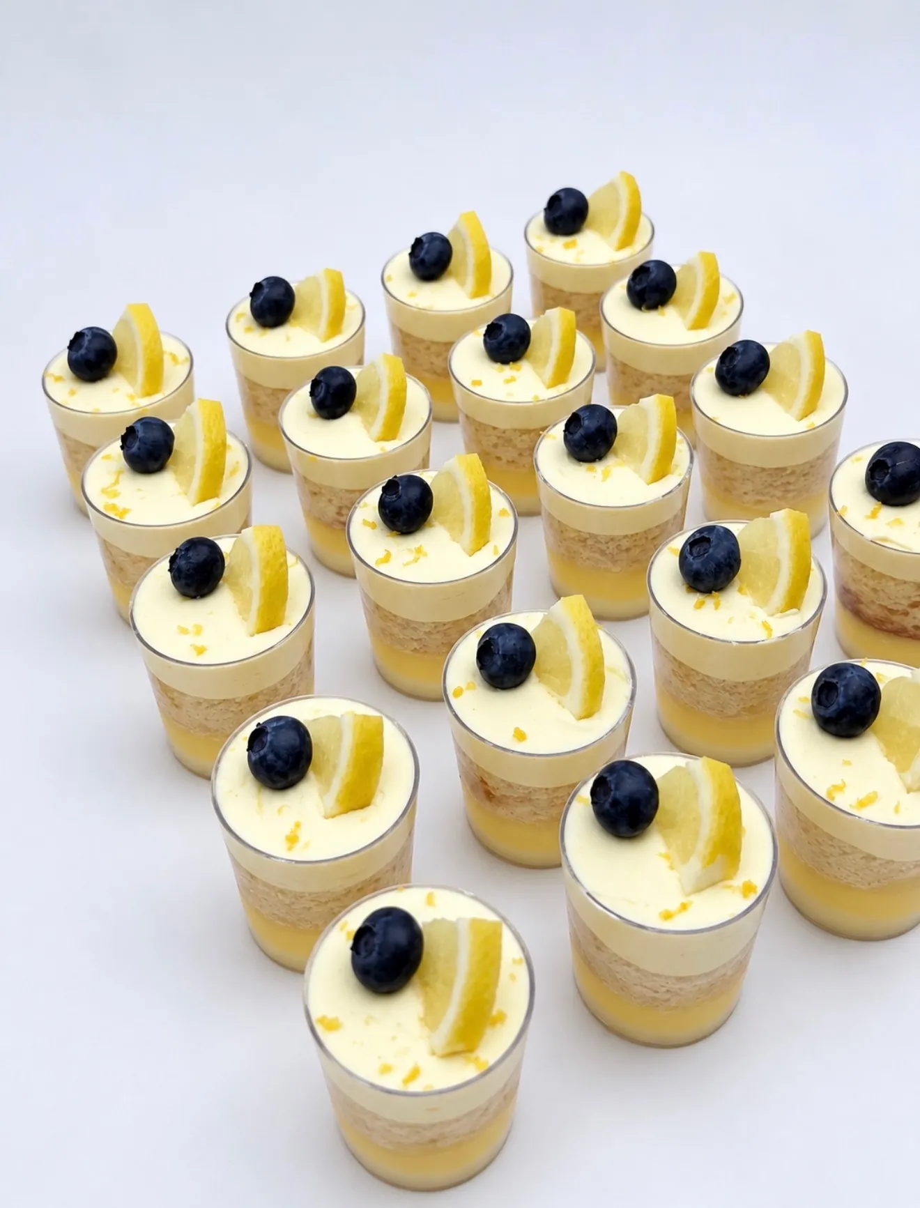 Lemon blueberry mini dessert shooters with lemon curd and cream, each topped with a blueberry and a lemon wedge