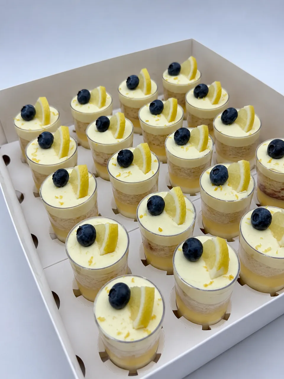 Lemon mini dessert shots topped with fresh blueberries, lemon slices, and lemon zest