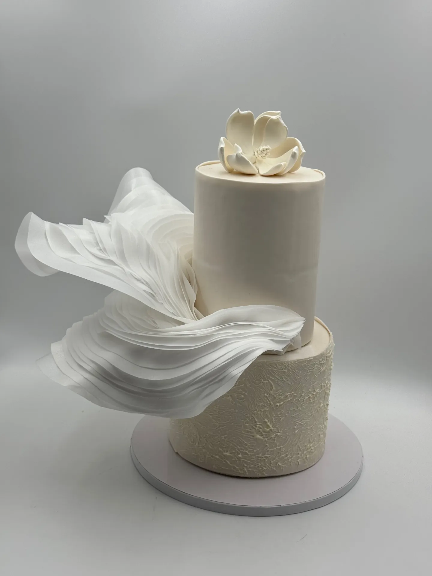 Minimalist white two-tier wedding cake with a sculptural sugar sail