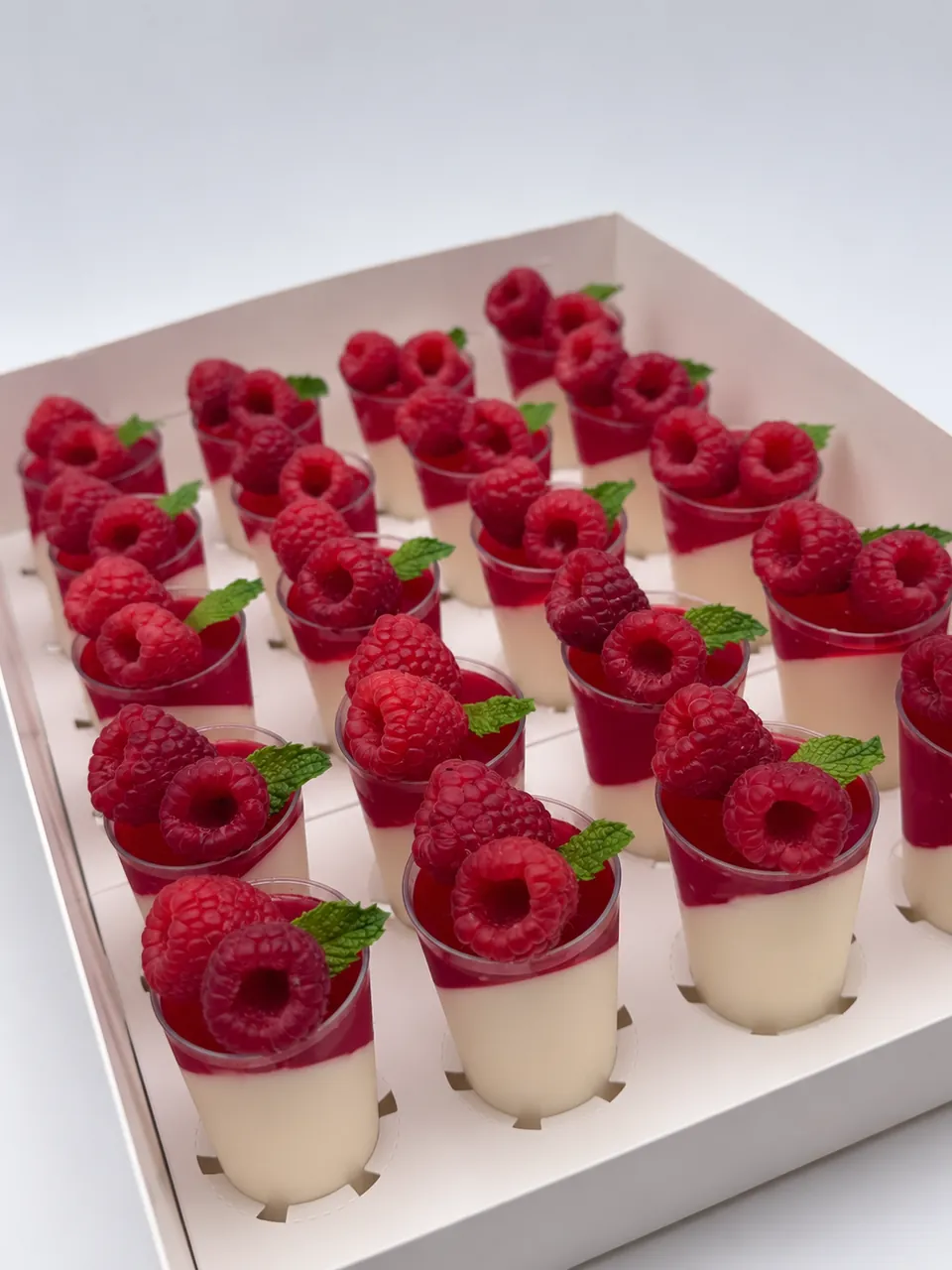 Panna cotta mini dessert shots topped with raspberry jelly, fresh raspberries, and mint