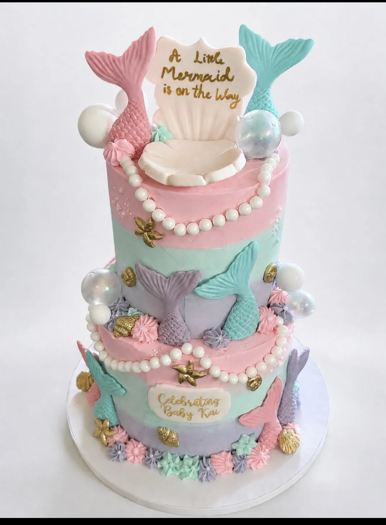 Two-tier pastel mermaid baby shower cake with fondant tails, seashells, pearl strands, and bubbles