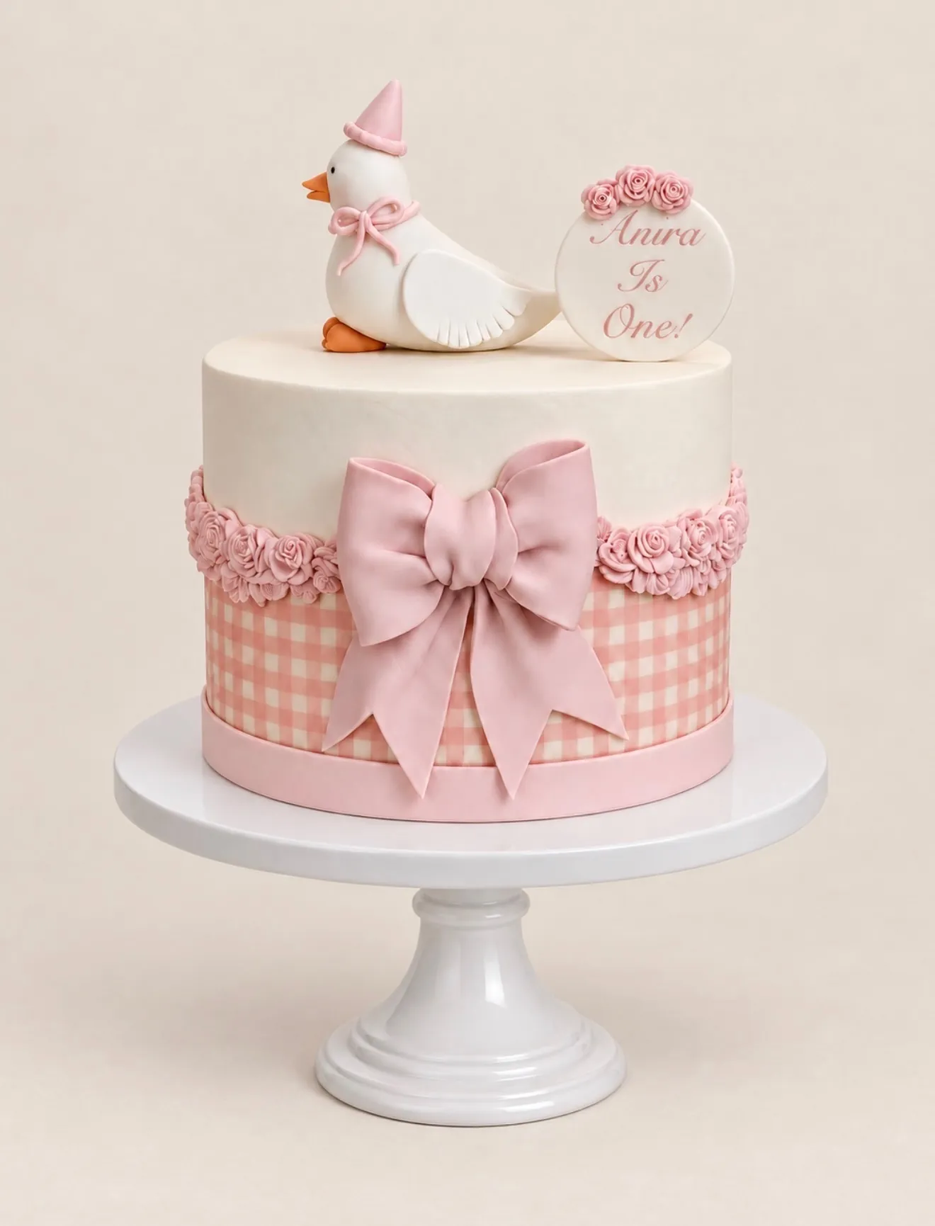 First birthday cake with pink gingham band, large pink fondant bow, rose trim, and a duck topper in a party hat
