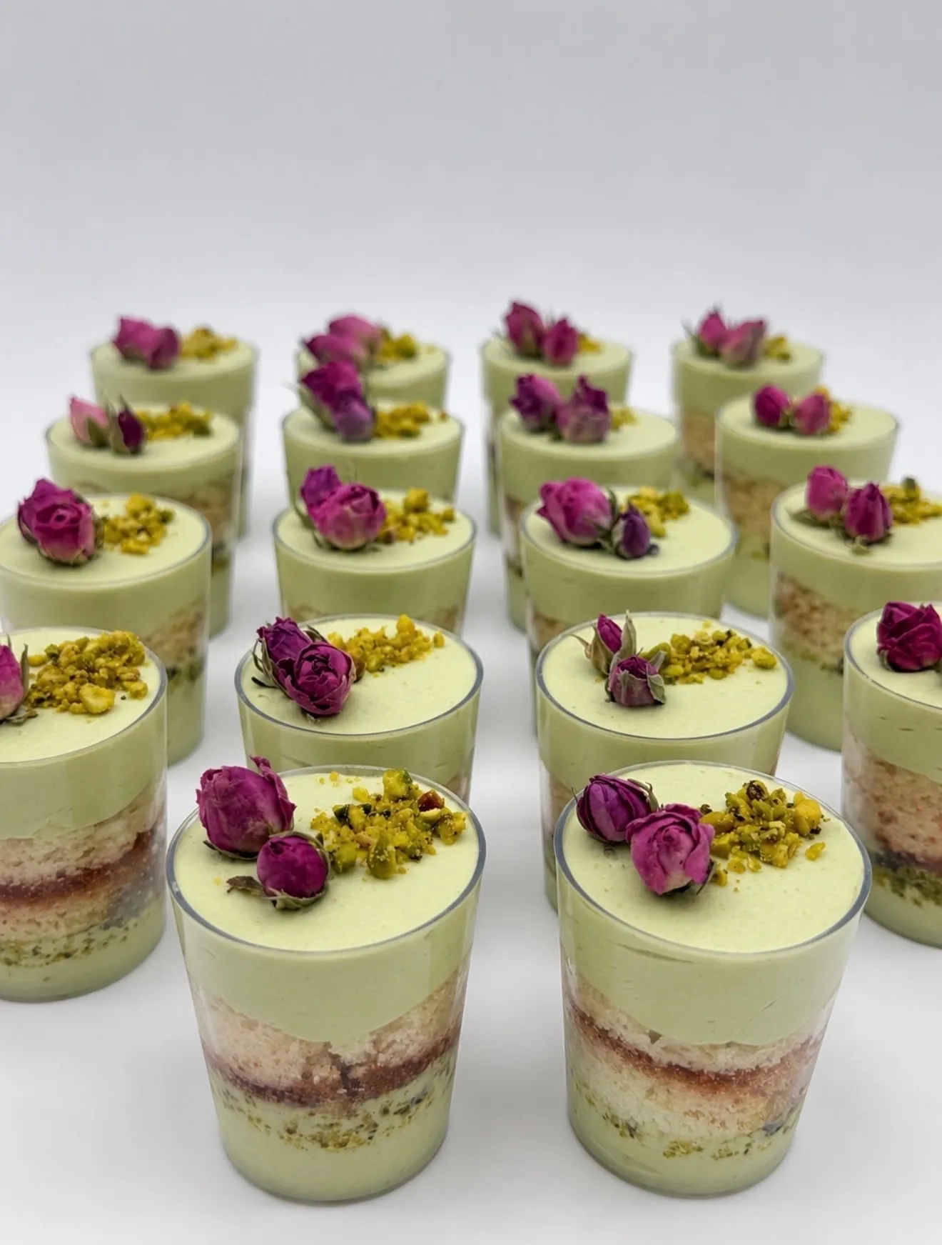 Pistachio rose mini dessert shooters layered with sponge and rose jam, topped with dried rosebuds and chopped pistachio