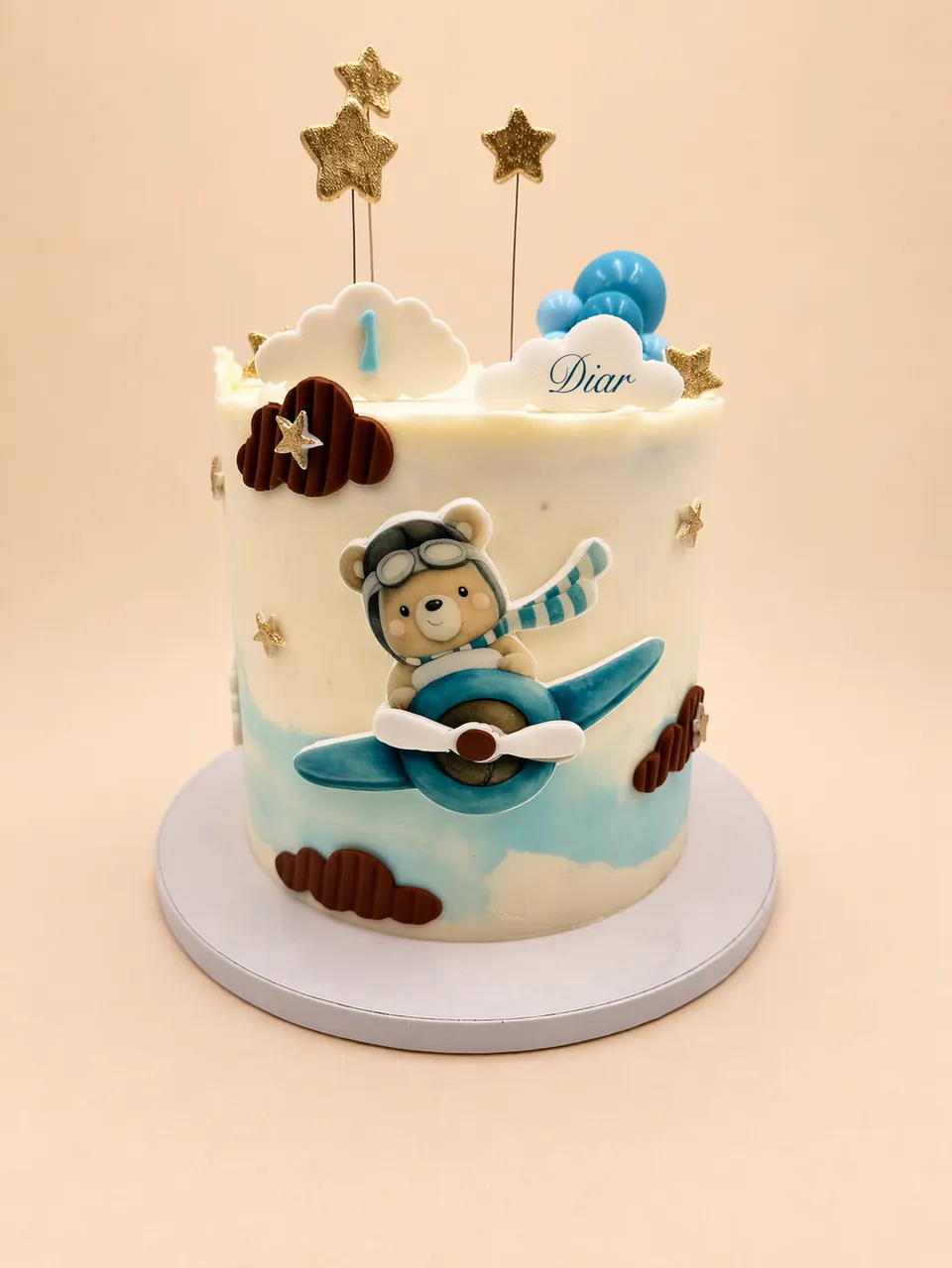 Teddy bear airplane first birthday cake with blue clouds and gold stars