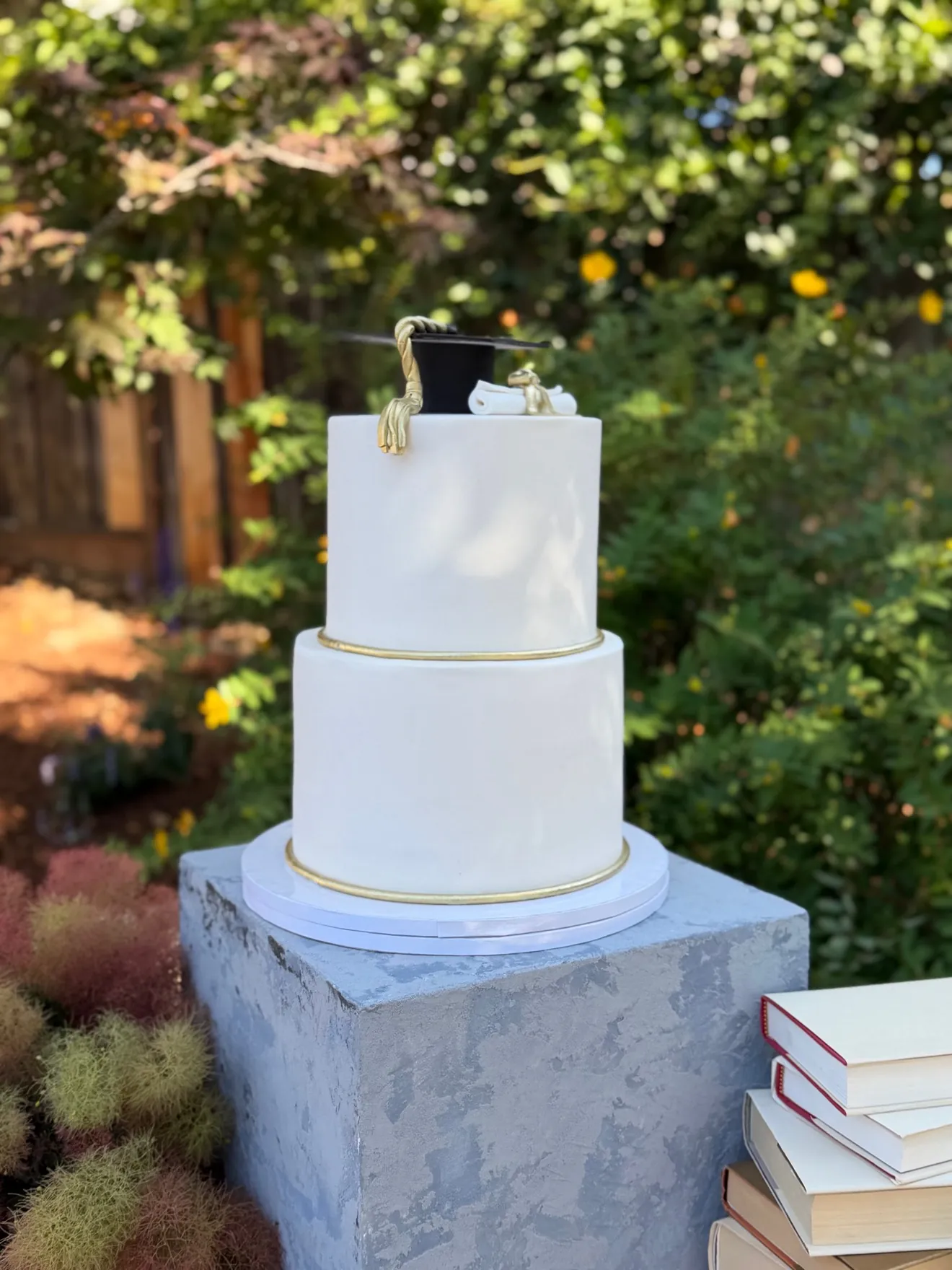 Two-tier graduation cake with cap, diploma, gold trim, and book display