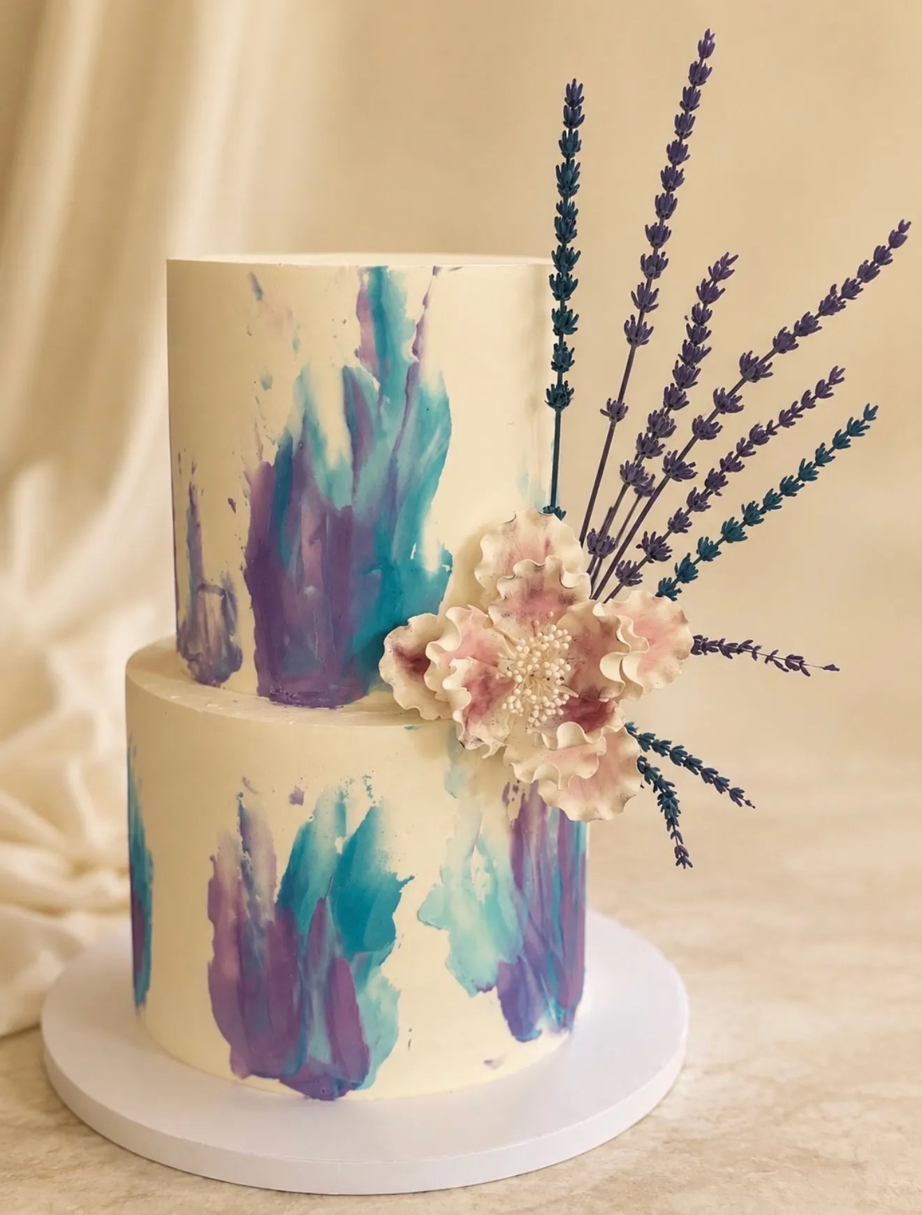 Watercolor two-tier custom cake with teal and purple buttercream, lavender stems, and sugar flower