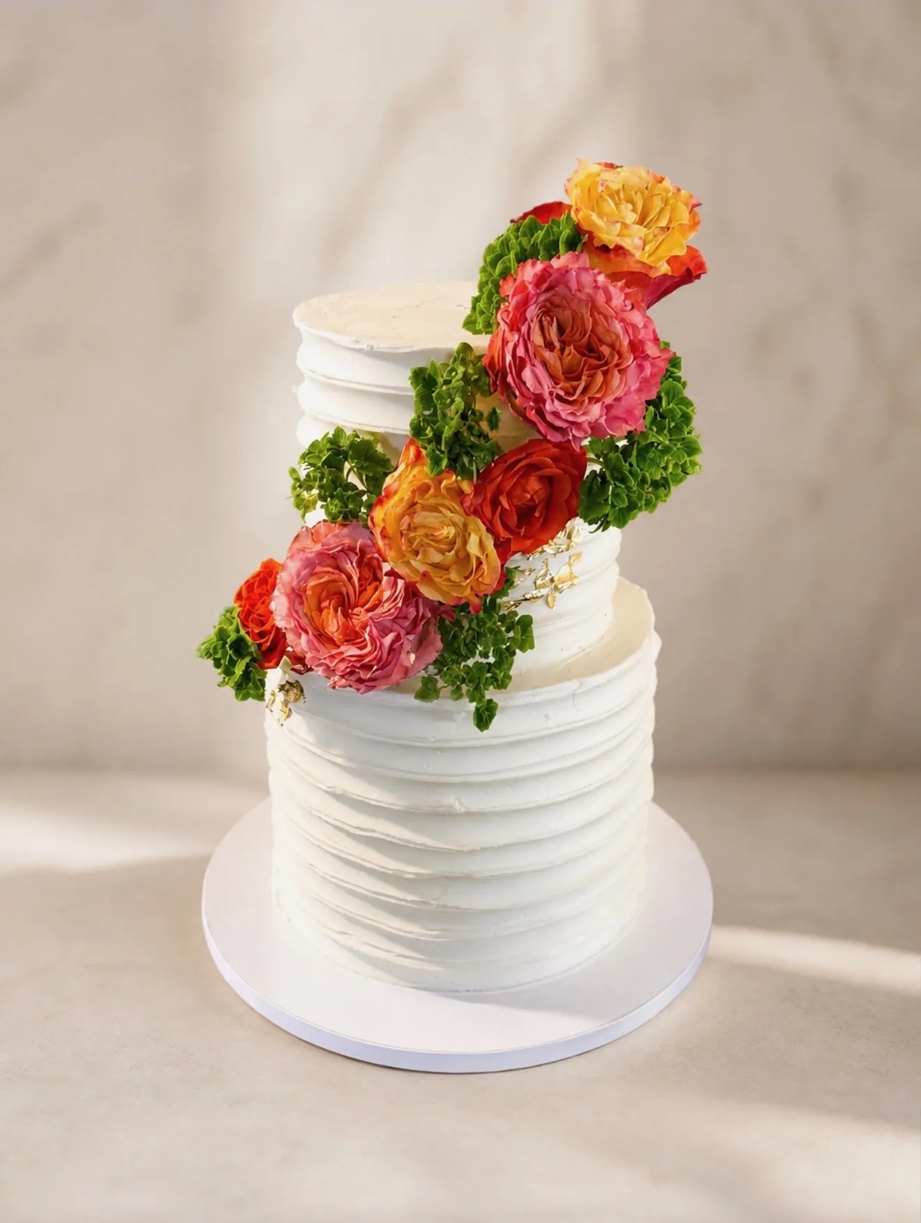 White buttercream wedding cake with cascading bright roses and greenery