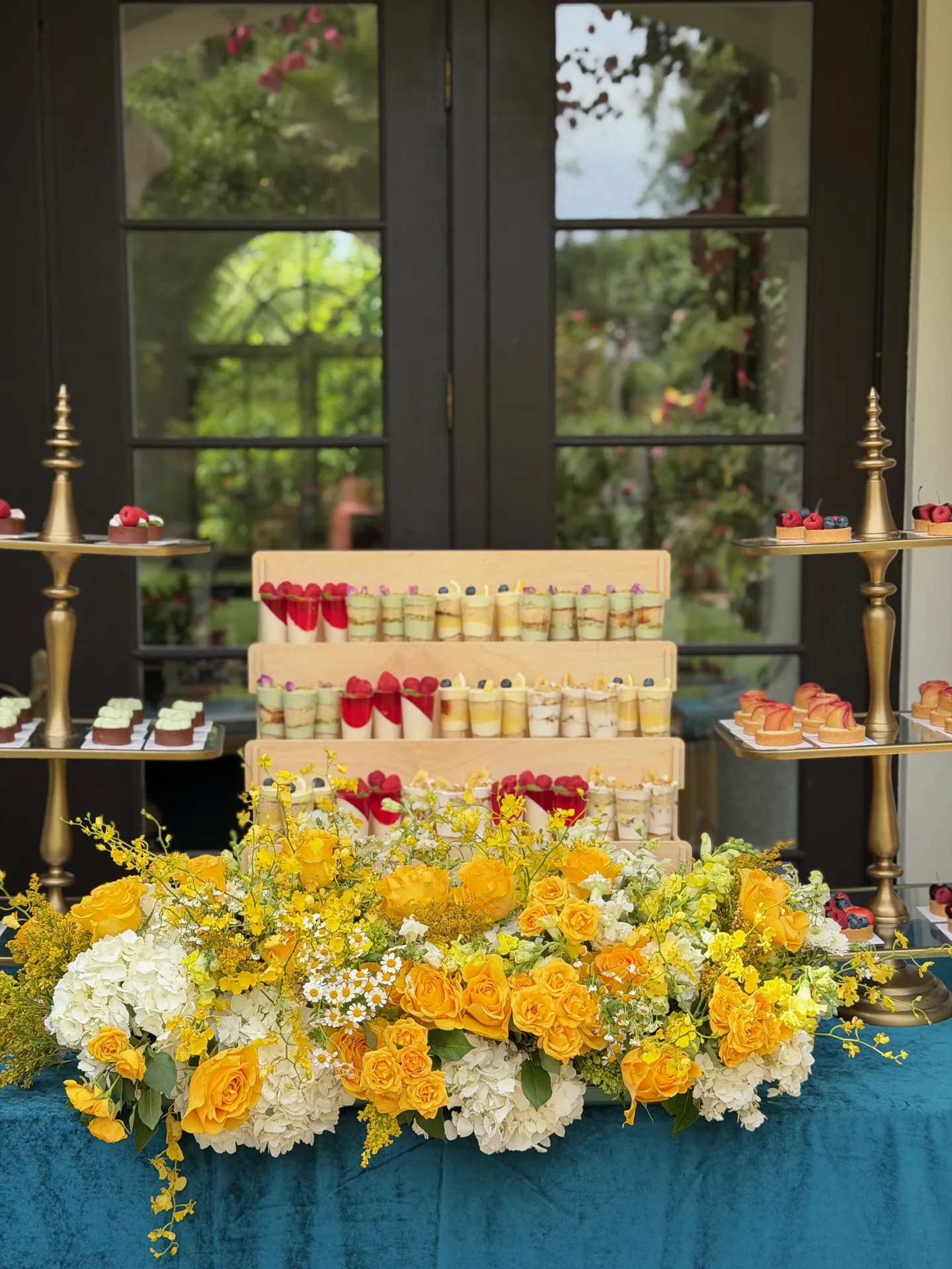 Mini dessert display behind a large yellow and white floral arrangement